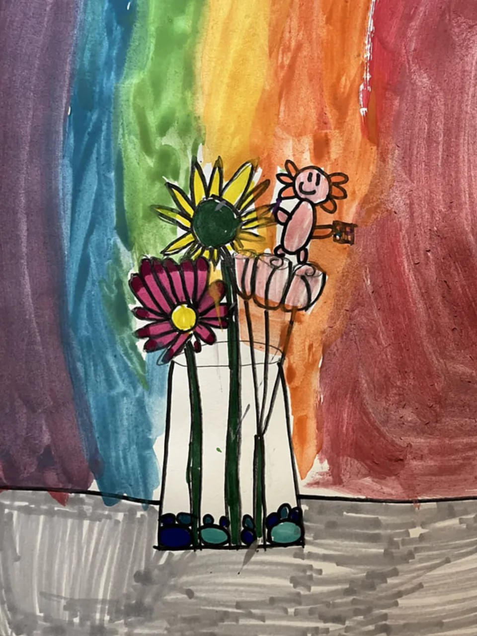 A child’s still life of flowers in a vase, drawn in crayon over a rainbow wash of paint.