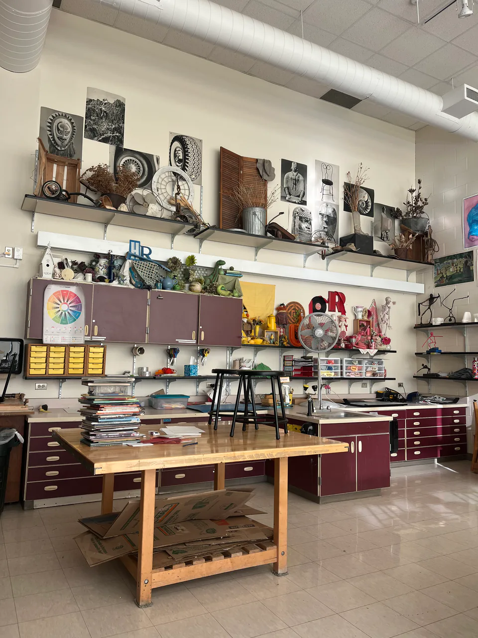 A high school art room with open shelving of supplies and long worktables.