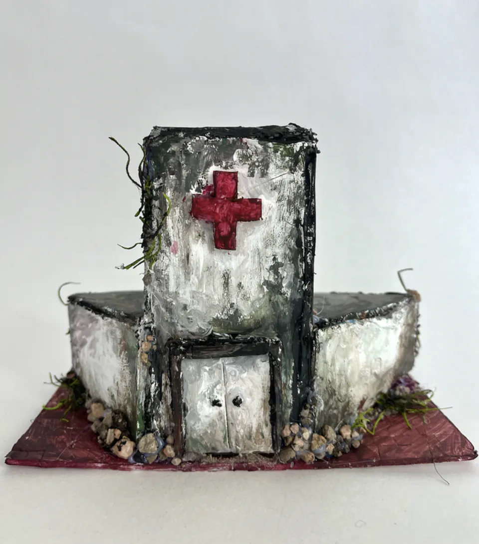 A foam core architectural model of a textured white building marked with a red cross.