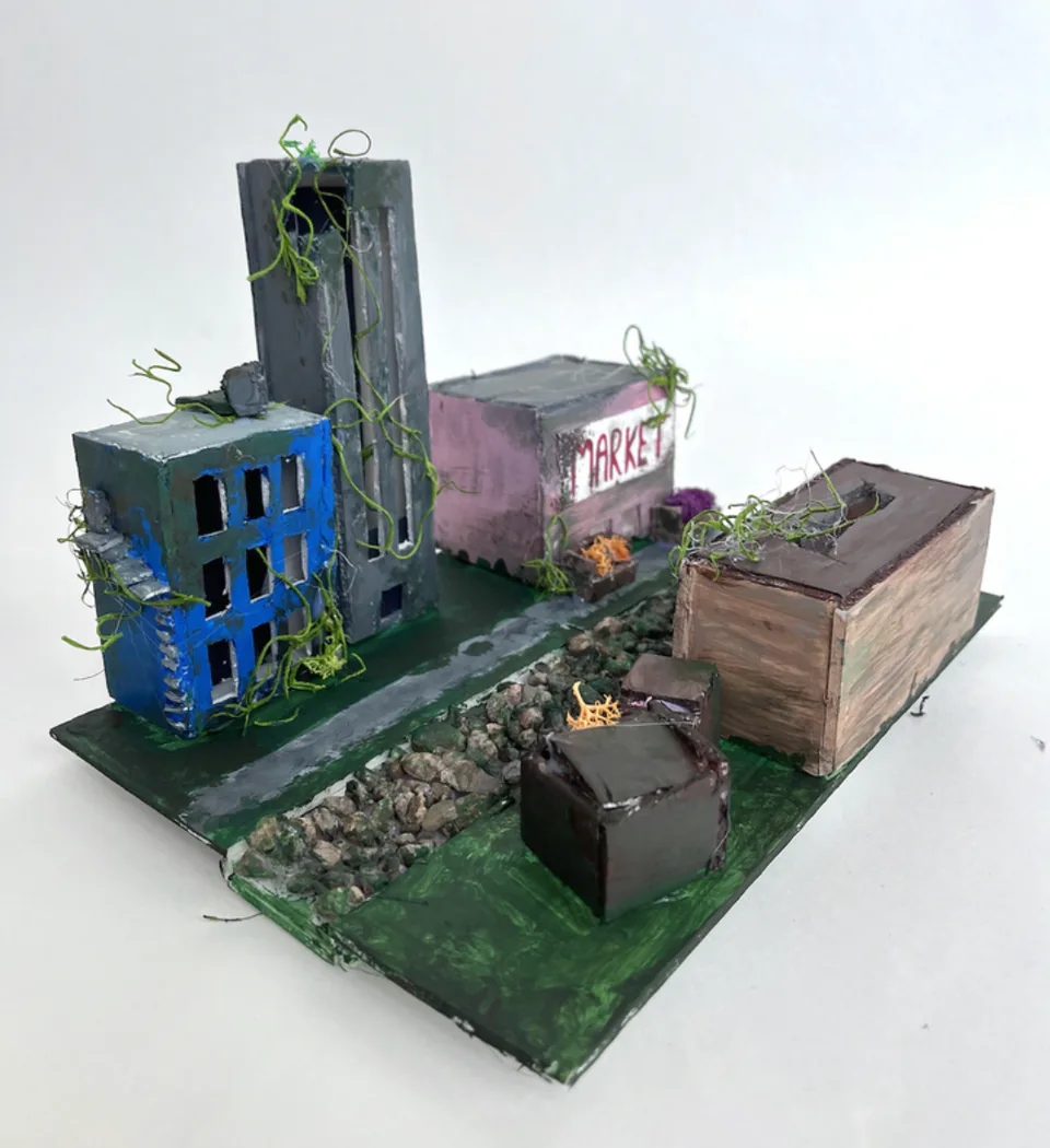 A foam core architectural model of a city block with green and pink buildings and small signage.